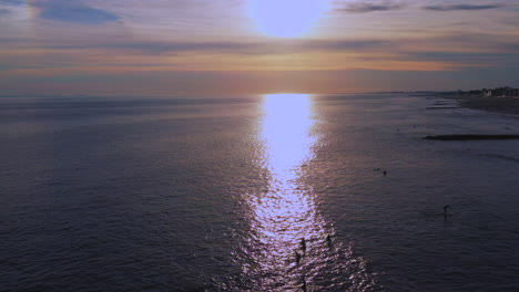 Dolly-En-Lo-Alto-Se-Disparó-Hacia-Adelante,-Descendió-Sobre-Los-Surfistas-En-El-Océano-Atlántico,-La-Cámara-De-Drones-Se-Movió-Hacia-Una-Puesta-De-Sol-Dorada