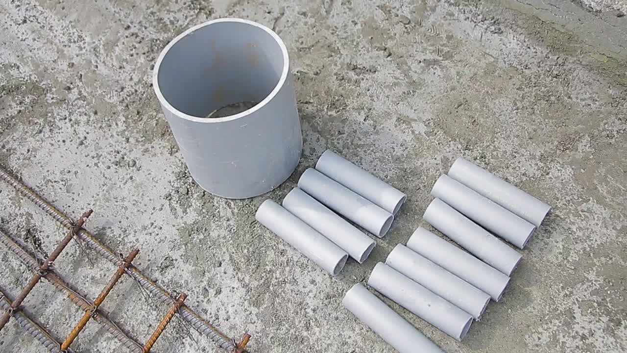 Large PVC pipe and smaller segments laid out next to steel reinforcement mesh on a construction site