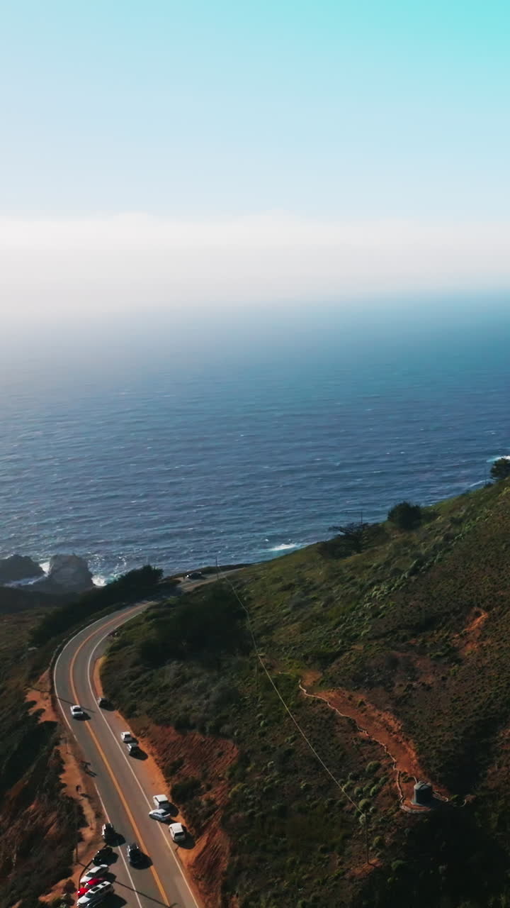 Rising along the sloping mountain covered with green grass. Highway at the foot of a mountain and house at top. Splendid view of an ocean merging with skies. Vertical video