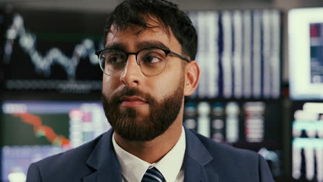 a businessman in a suit and tie looks seriously at a chart on a computer screen in a stock market office.