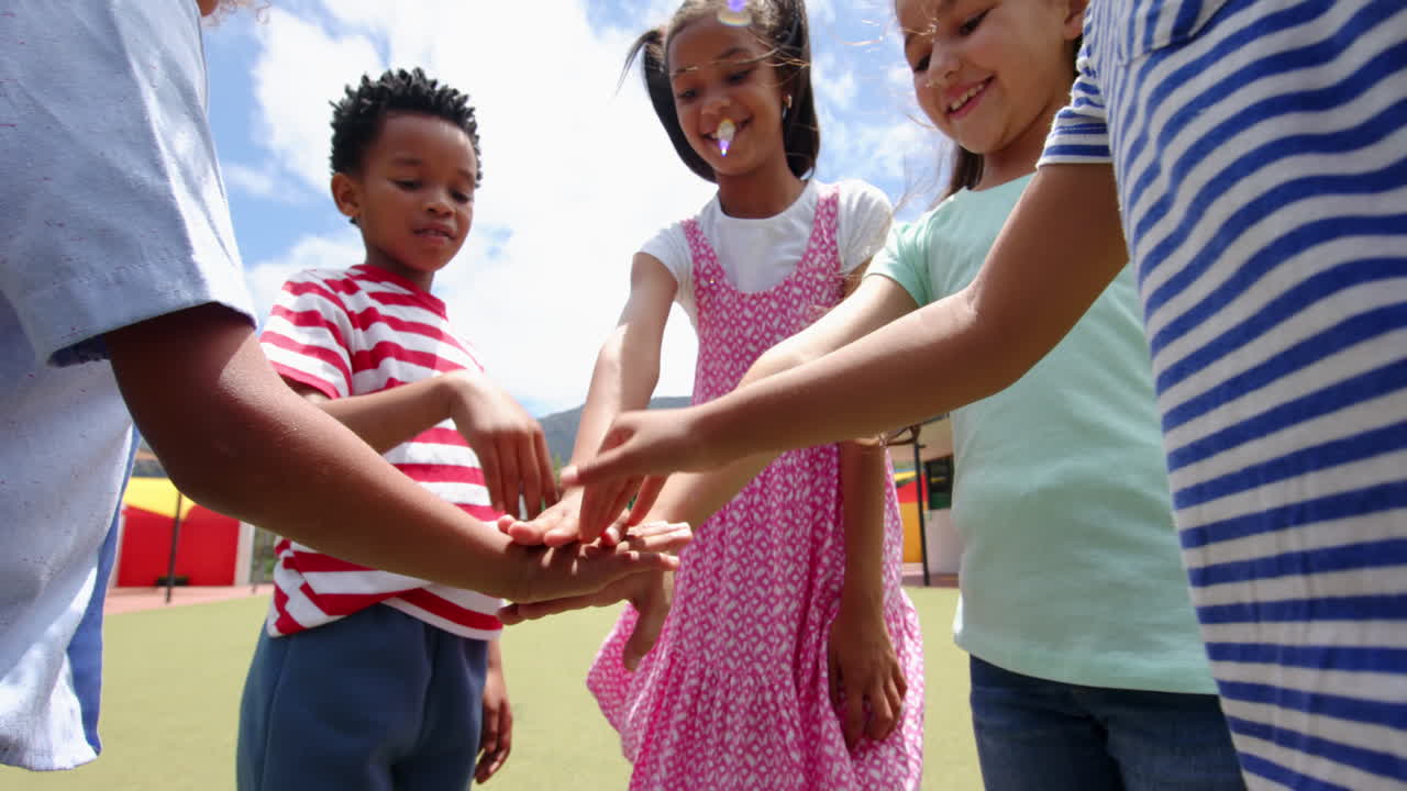 In schoolyard, children stacking hands, showing teamwork and unity