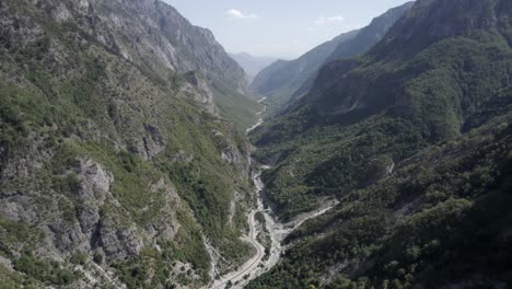 Drohnenvideo-Eines-Frontal-Absteigenden-Flugzeugs-Zwischen-Den-Hügeln-Des-Valbone-Tals-Und-über-Der-Straße-Azem-Hajdariy-Und-Dem-Fluss