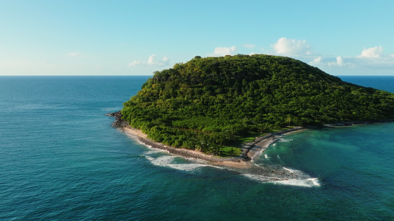 Drone orbiting a small uninhabited Guadeloupe island, showing forested hills and waves on the shore
