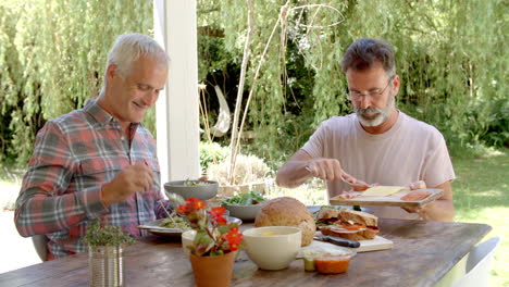 homosexual couple at home eating meal on outdoor verandah