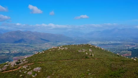 Arial-drone-view-of-hill-top-with-mountains-in-distance-and-houses-in-valley-below,-Paarl-South-Africa