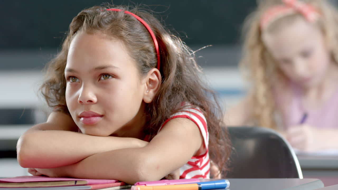 In school, girl daydreaming at desk while another student writing in classroom