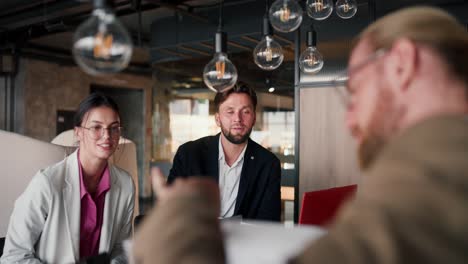 close-up shot of a blond man wearing glasses in light brown, his solution to a problem and showing his colleagues his idea on paper. colleagues communicating at the workplace in a modern office. girl in a light suit and a brunette guy