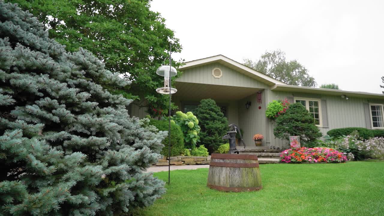 Beautiful front yard of a house with gorgeous plants and flowers out front and a antique water pump