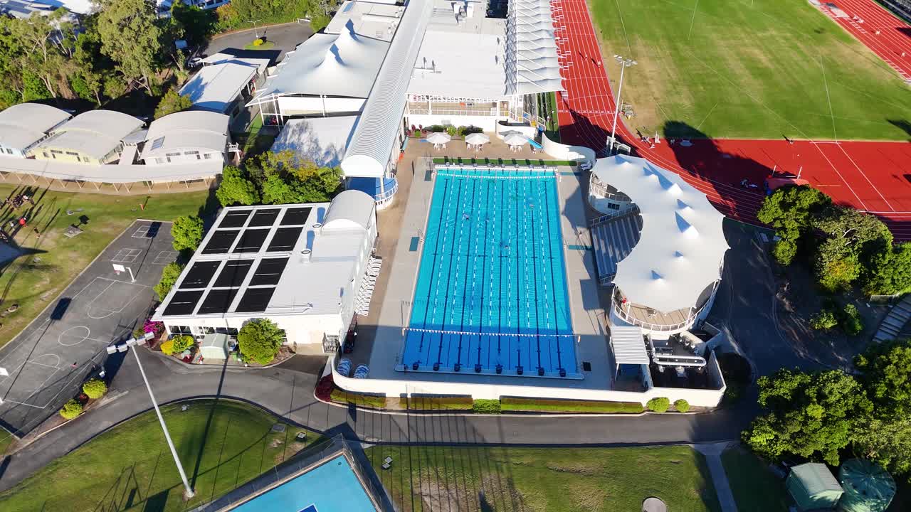 Drone footage captures a vibrant sports park with pools, fields, and tracks in Gold Coast, Australia under bright daylight