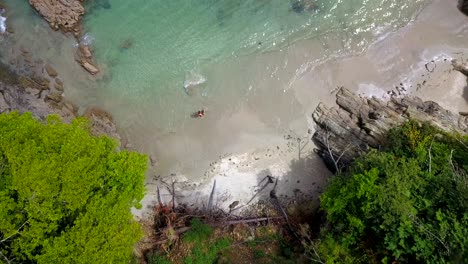 Aerial-Overhead-View-Of-Couple-Walking-Into-Waters-From-Secluded-Cove-Beach