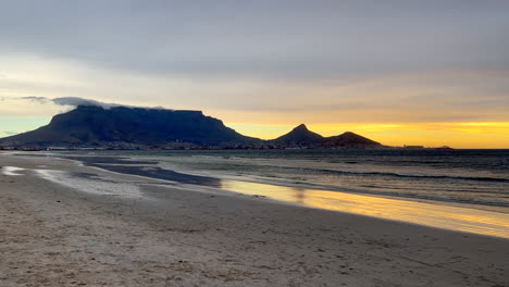 Stunning-Cape-Town-Table-Mountain-beach-landscape-golden-yellow-orange-sunrise-sunset-South-Africa-low-tide-wind-at-sea-ocean-incredible-coastline-slow-motion-pan-to-the-right