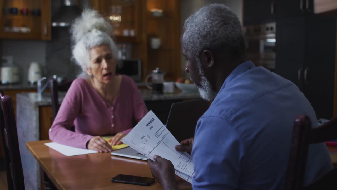 pareja de ancianos de raza mixta discutiendo y calculando las finanzas en casa