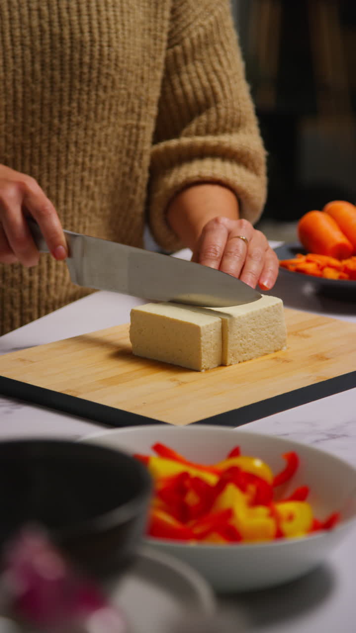 Vertical Video Close Up Of Woman At Home In Kitchen Preparing Healthy Vegetarian Or Vegan Meal Slicing Tofu On Board With Knife