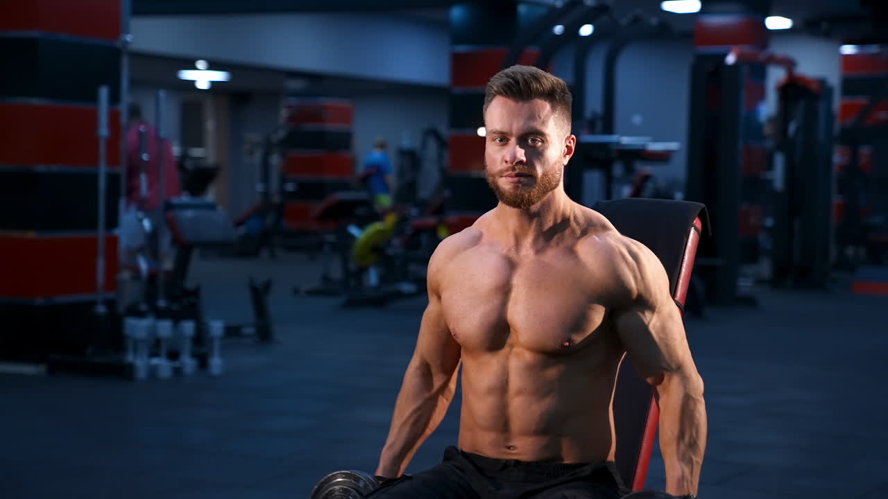Handsome power athletic man bodybuilder doing exercises with dumbbells. Fitness muscular body on dark gym background.