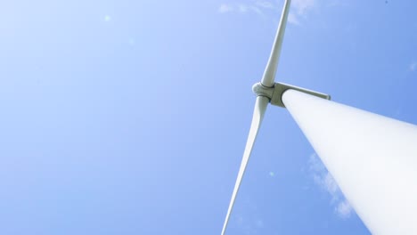 Looking-up-below-wind-turbine-energy-generator-spinning-blades-and-sunny-blue-sky