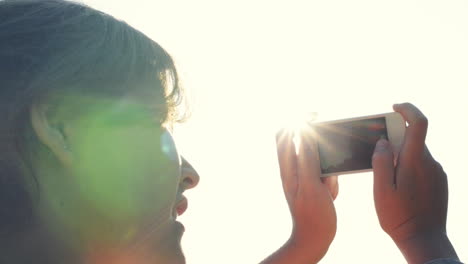 woman taking photographs using mobile phone sunset