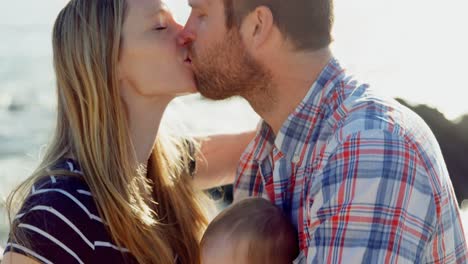 Side-view-of-mid-adult-caucasian-parents-kissing-each-other-at-beach-on-a-sunny-day-4k