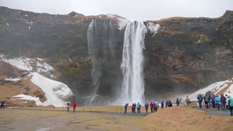 plano estático, amplio, de muchas personas paradas frente y disfrutando de la vista de la cascada seljalandfoss, en un día nublado de otoño, en islandia