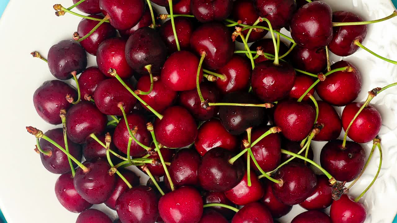 Cherries rotate on a plate on a blue background. Lots of ripe juicy cherry. Vitamins, vegan, fruit food video concept
