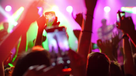 concert crowd with raised hands and smartphones capturing vibrant stage performance atmosphere