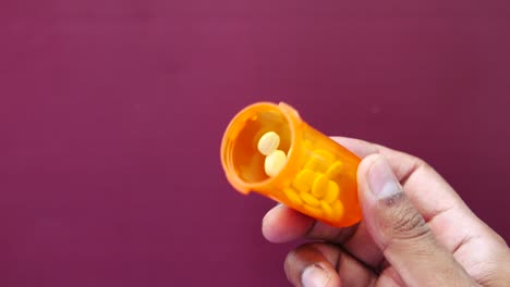 persona sosteniendo un frasco de pastillas naranja con pastillas amarillas