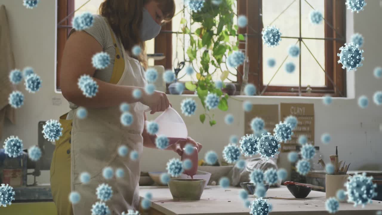 코로나19 세포의 애니메이션 도자기 스튜디오에서 일하는 여성이 얼굴 마스크를 쓰고 있습니다.