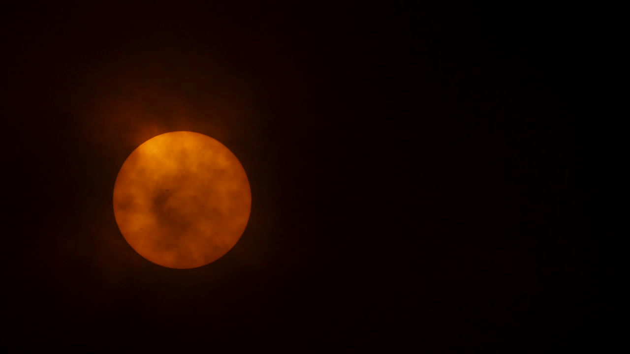 Close up of the sun behind heavy clouds, sun spots visible on the surface