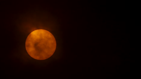 Close-up-of-the-sun-behind-heavy-clouds,-sun-spots-visible-on-the-surface