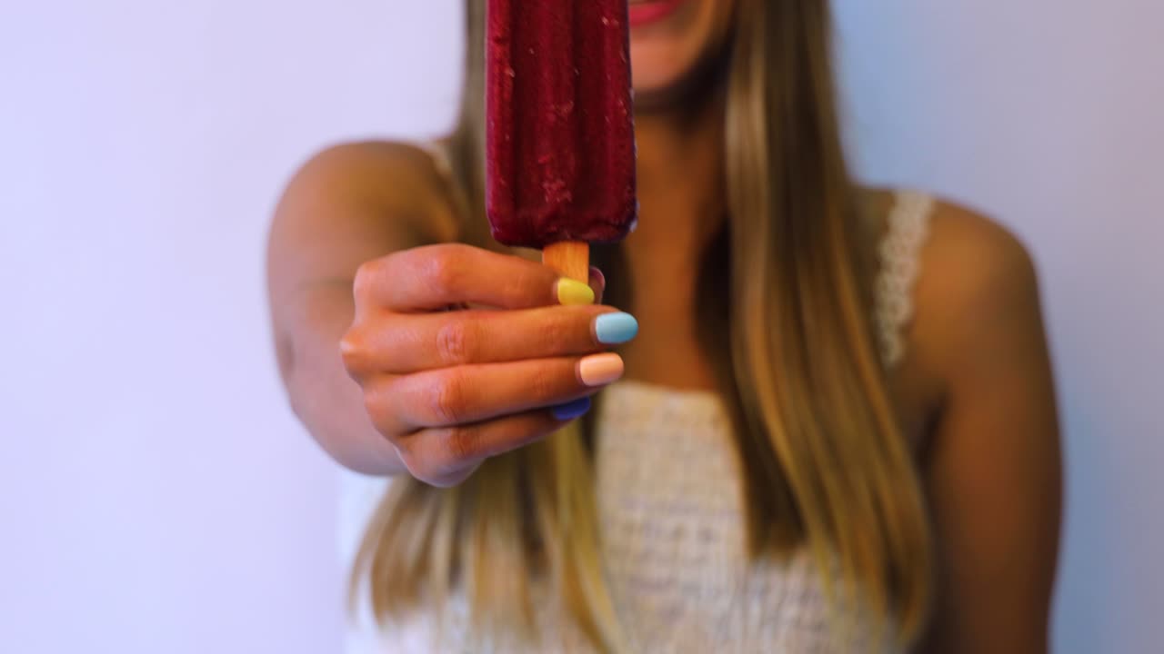 niña sonriente sosteniendo un helado rojo con uñas coloridas