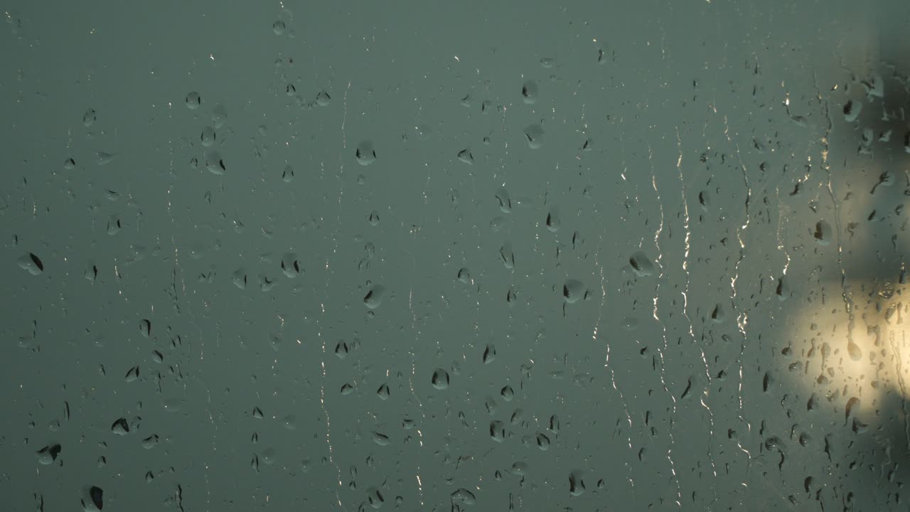 Raindrops on the window pane. A lantern can be seen outside the window.