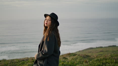 woman standing cloudy seacoast in front gray ocean waves. girl posing on shore.