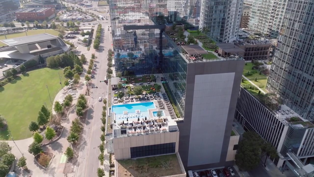 Grabación aérea con dron capturando el hotel más grande a lo largo del paseo ribereño, con el anfiteatro y el parque de fondo, incluyendo una piscina en la azotea y jardines