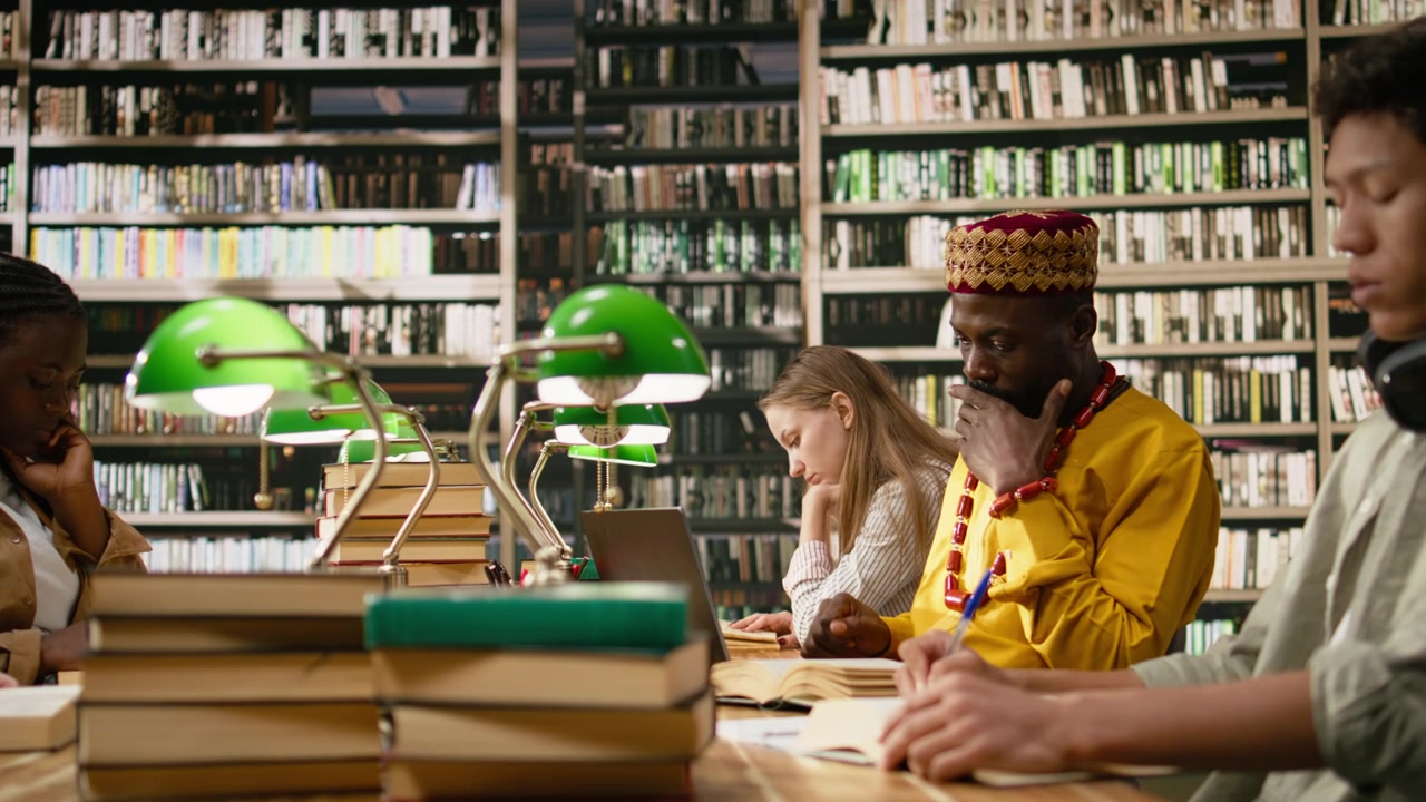 Studente maturo africano in abiti tradizionali gialli che lavora al laptop.