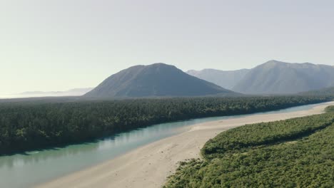 Toma-Panorámica-Aérea-De-Izquierda-A-Derecha-De-Un-Río-Con-Una-Cadena-Montañosa-En-El-Fondo-En-La-Costa-Oeste-De-Nueva-Zelanda