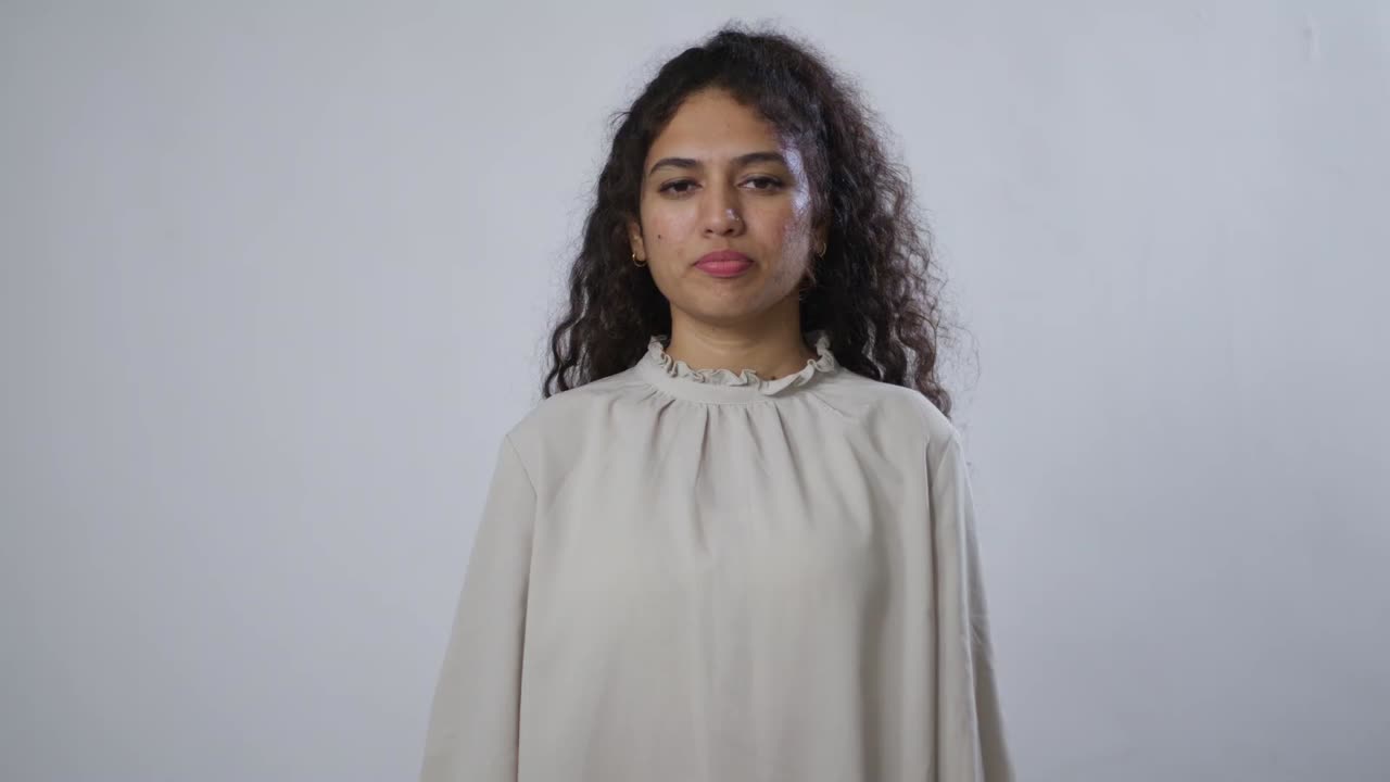 Uma jovem sul-asiática com cabelos castanhos e cacheados segura o pescoço com uma expressão de dor
