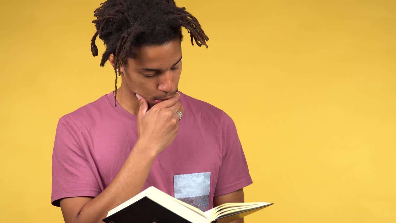 Thoughtful young black student reading a book, studio yellow background