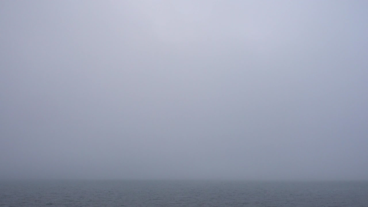 Thick fog over morning calm water surface, looped video.