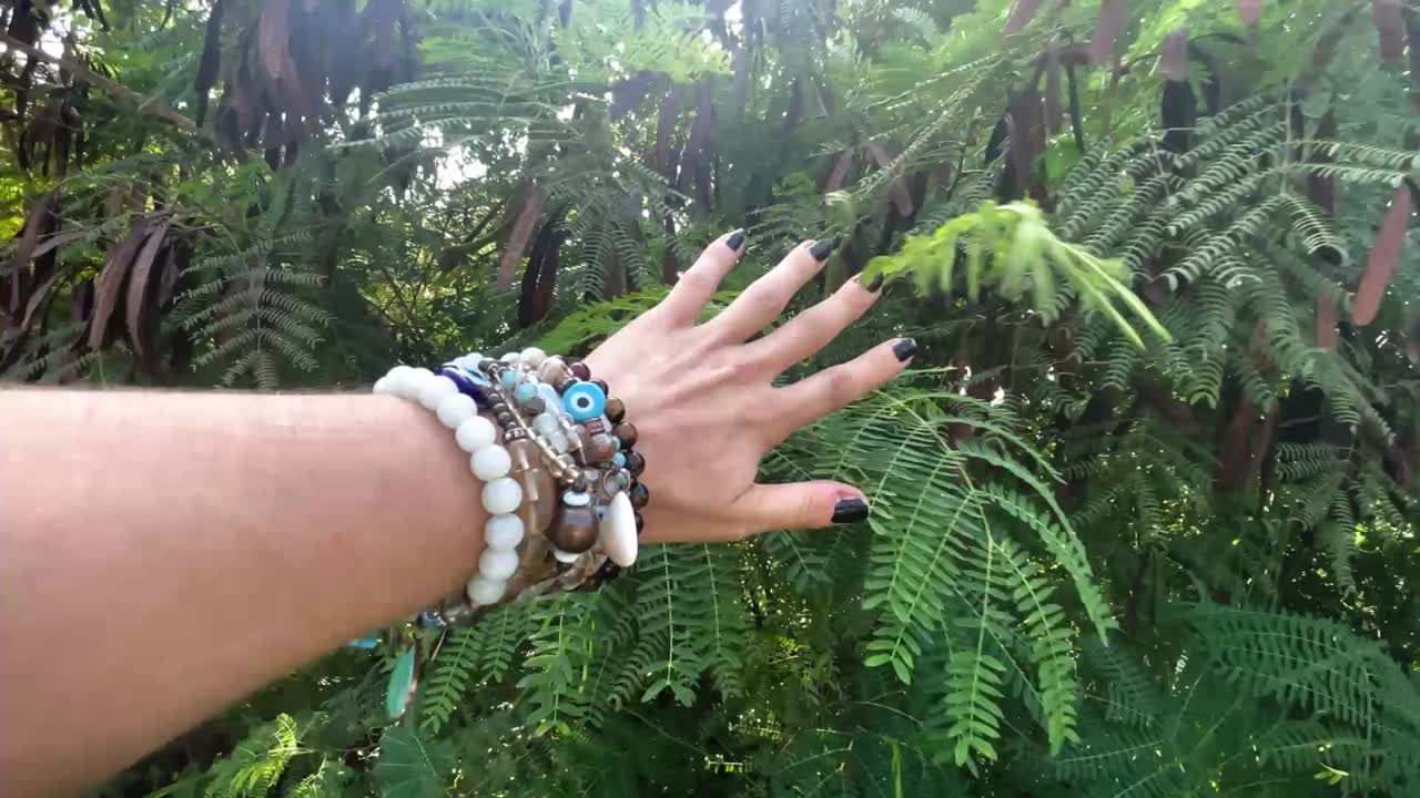Woman reaching out to nature, lush greenery, and bracelets.