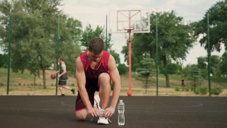 in foreground, male basketball player kneeling and tying his shoeslaces