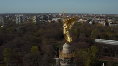 AERIAL:-Close-Up-Circling-around-Berlin-Victory-Column-Golden-Statue-Victoria-in-Beautiful-Sunlight-and-Berlin,-Germany-Cityscape-Skyline-in-Background