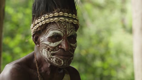 close up shot, indigenous man face painted, and adjusting clam headdress.