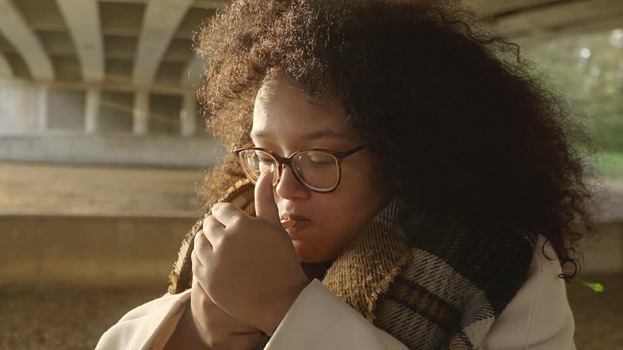 Black woman with curls lighting up a sigaret underneath a bridge during sunset