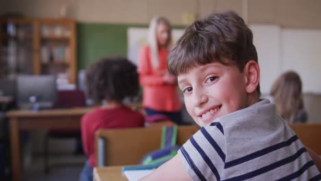 Boy-smiling-while-sitting-on-his-desk-at-school