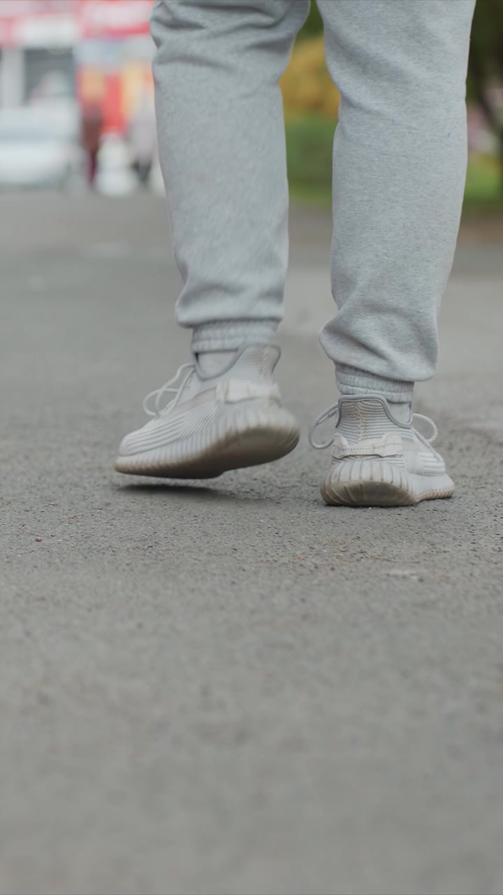 Person in light gray sweatpants and white sneakers walking. White shoes contrast slightly due to accumulated grime. Outdoor scene captures movement against softly blurred