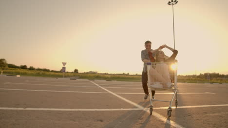 Lens-flare:-Cheerful-people-couple-man-and-woman-at-sunset-ride-supermarket-trolleys-in-slow-motion.