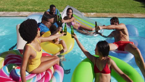 diverse group of friends having fun playing on inflatables making a toast in swimming pool