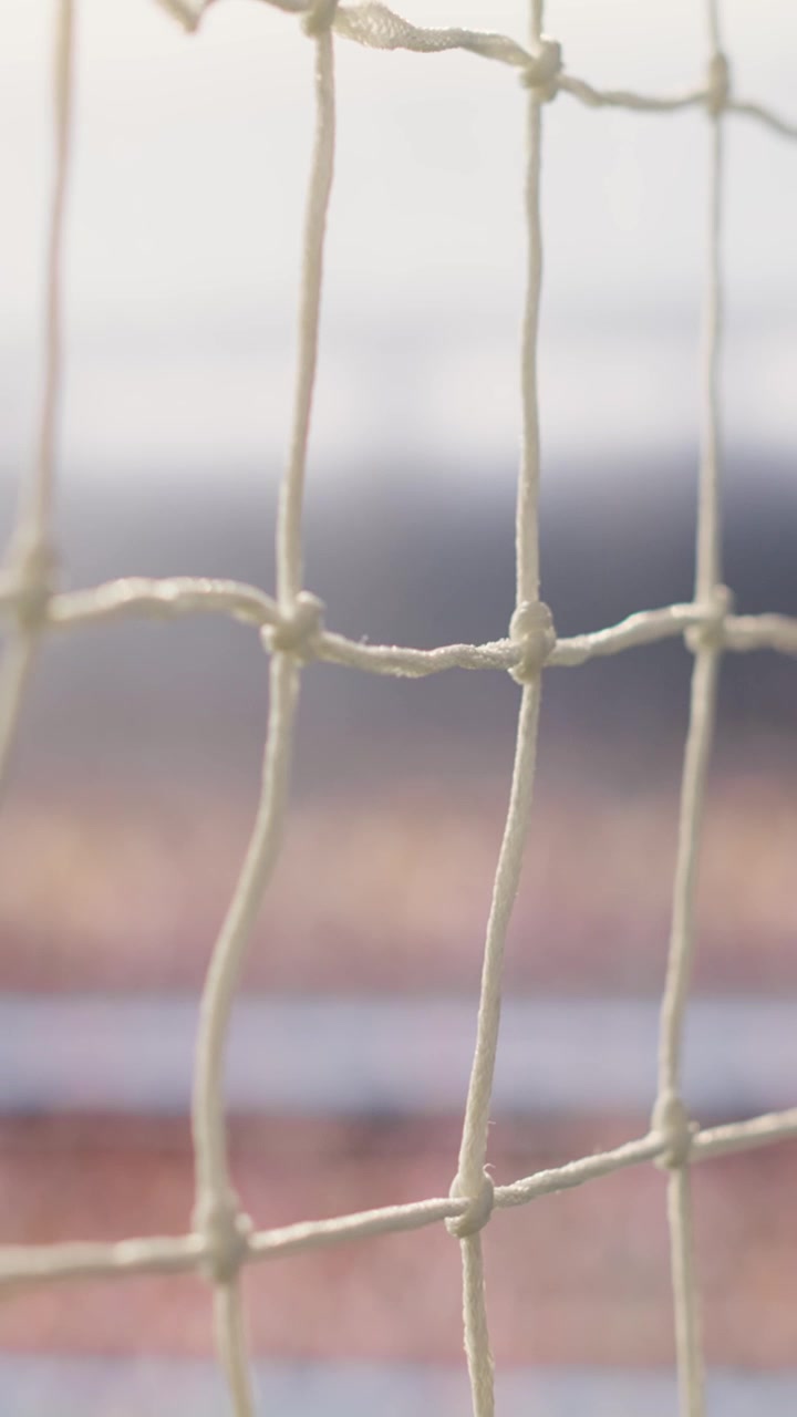 Video verticale. Dettaglio della rete e del palo della porta con messa a fuoco selettiva su un campo da calcio sotto la luce dello stadio.