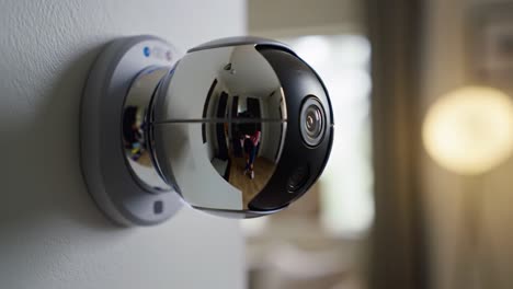a modern, spherical security device is mounted on the wall in a well-lit living room. the camera reflects various details of the room while monitoring the environment.