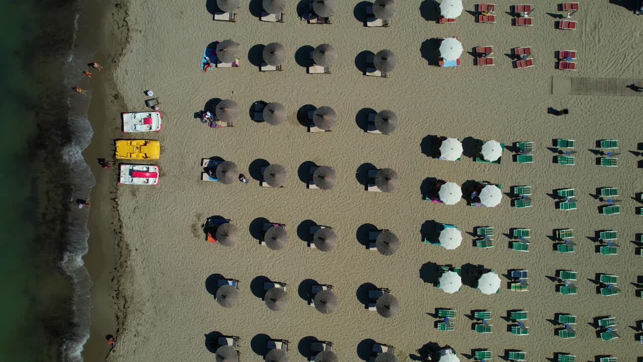 Colorful beach umbrellas and sunbeds lined up on sandy beach, lapped by salty waters of shallow lagoon, Adriatic Sea, Durres, Albania