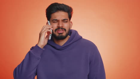 tired sleepy indian man talking on smartphone with friend, making online conversation, boring talk